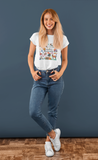Blonde girl with jeans wearing a white country romantic tee in front of a blue wall