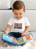 Little boy looking at a children's book while wearing a Robo DJ white t-shirt