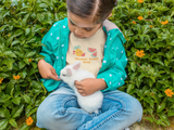 Little girl with a bunny sitting in flowers wearing a natural color Flavor fruit day t-shirt