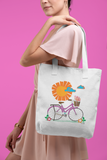 Sunny Bike Ride Organic Tote in natural color that shows a cute pink bike in front of a large orange sun worn by a women in front of a pink background