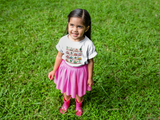 little girl wearing a white cozy little beep t-shirt looking up while standing on grass.