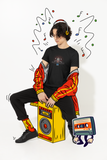 Louliibot tee with cute robot DJ graphic in the color black worn by a teen sitting on an ainimated speaker with music animation things around him