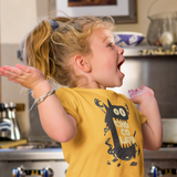 Tee shirt for kids with a cute monster that has his mouth open with the text chocolate in the middle in the color yellow worn by a young little girl laughing