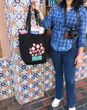 Manga Flower Organic Tote in black held by a woman in front of a mexican tile wall.