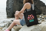 Manga Flower Organic whiteTote that has pink manga flowers in a flower box on a women's shoulder at the beach
