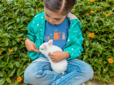 little girl sitting in flowers with a white rabbit while wearing a blue Friends Toddler T-shirt