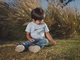Little boy sitting in the grass wearing a Space RoboDog Toddler T-Shirt 100% Organic t-shirt in light blue