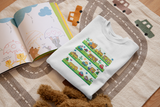 White cozy little beep t-shirt foled on a rug with a children's book