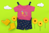 Flavor Fruit Day t-shirt in dark pink against a lime green wall with sun flowers and yellow boots