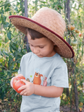 Little boy wearing a blue Friends t-shirt with a straw hat holding a tomato in the garden
