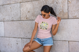 Young women with a Tropical Chic Loulii designed pink t-shirt leaning against a wall