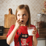 Tee shirt for kids with a cute monster that has his mouth open with the text chocolate in the middle in the color red worn by a child eating cookies and milk