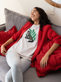 Fox tails tee that shows a black fox in front of green flora in the color white worn by a young woman relaxing on a couch smiling